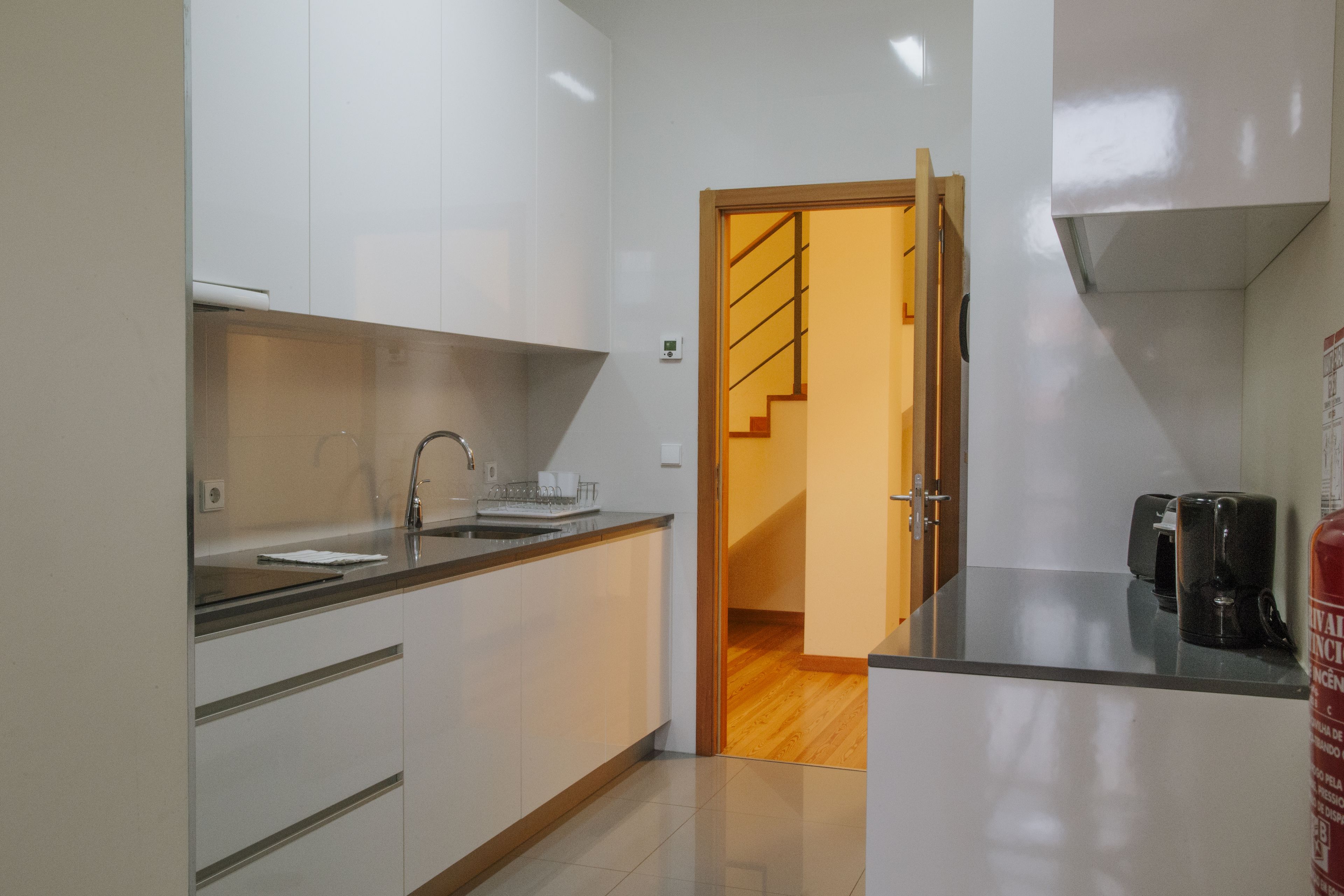 A modern kitchen with white cabinets, a stainless steel sink, and a coffee machine.