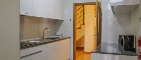 A modern kitchen with white cabinets, a stainless steel sink, and a coffee machine.