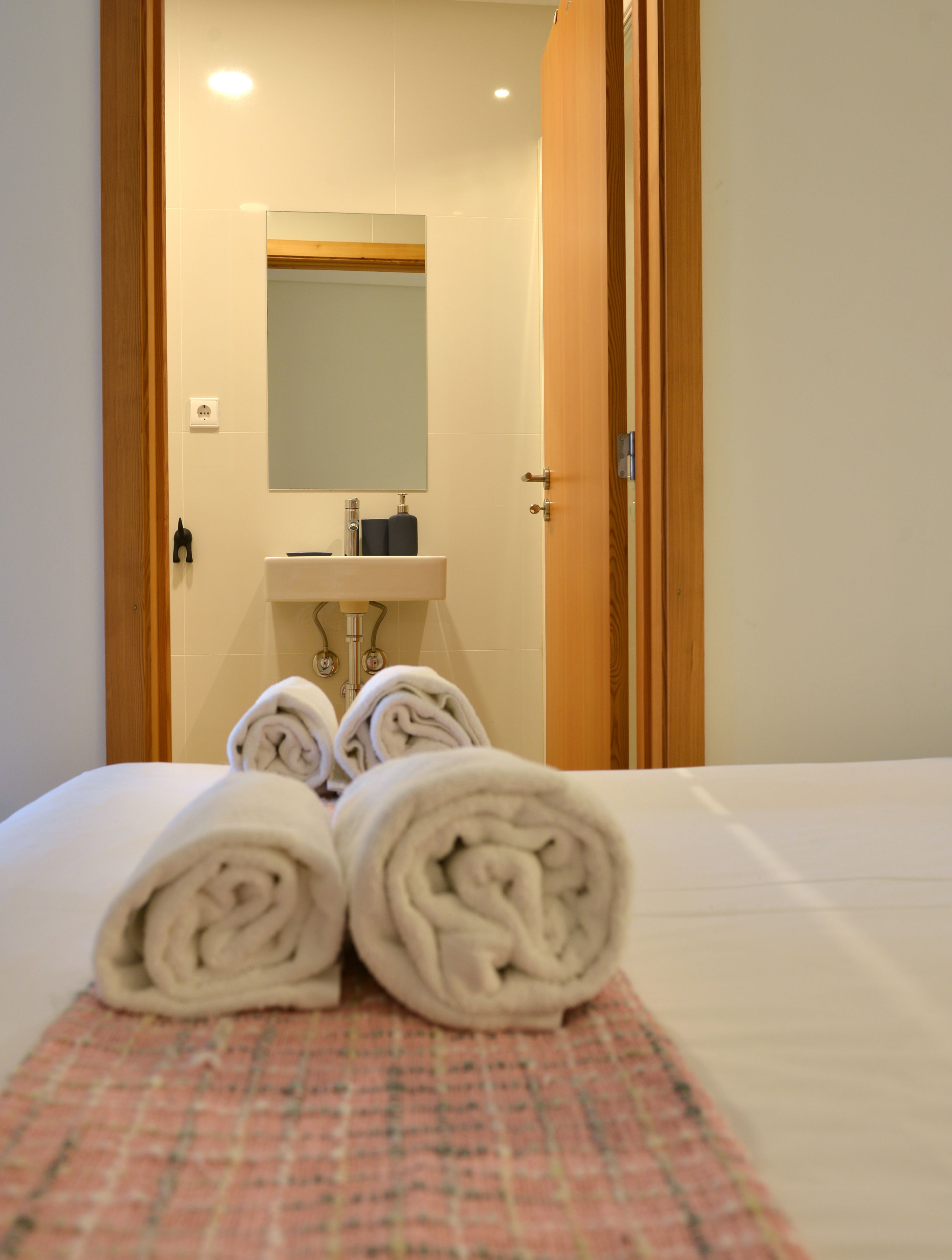 A hotel room with a bed, a bathroom with a sink and mirror, and towels on the bed.