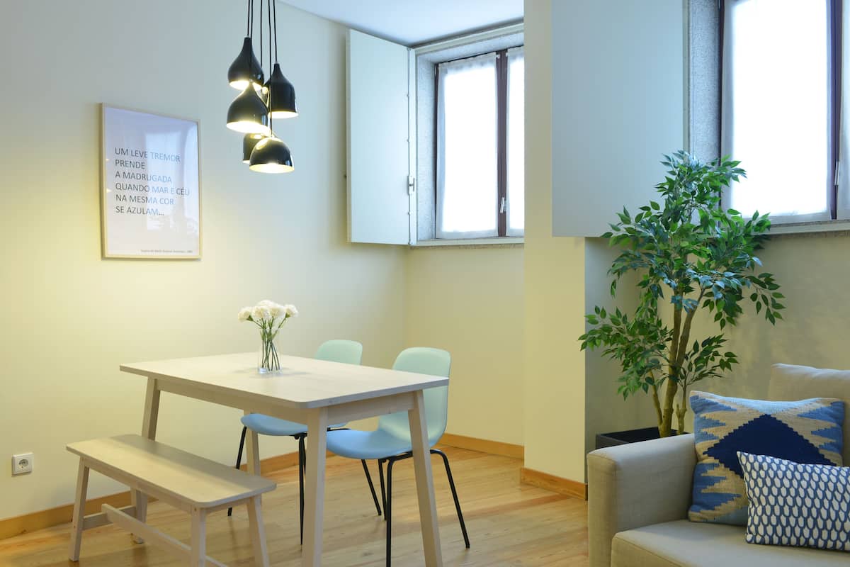 A modern living room with a dining area, a large window, and a potted plant.