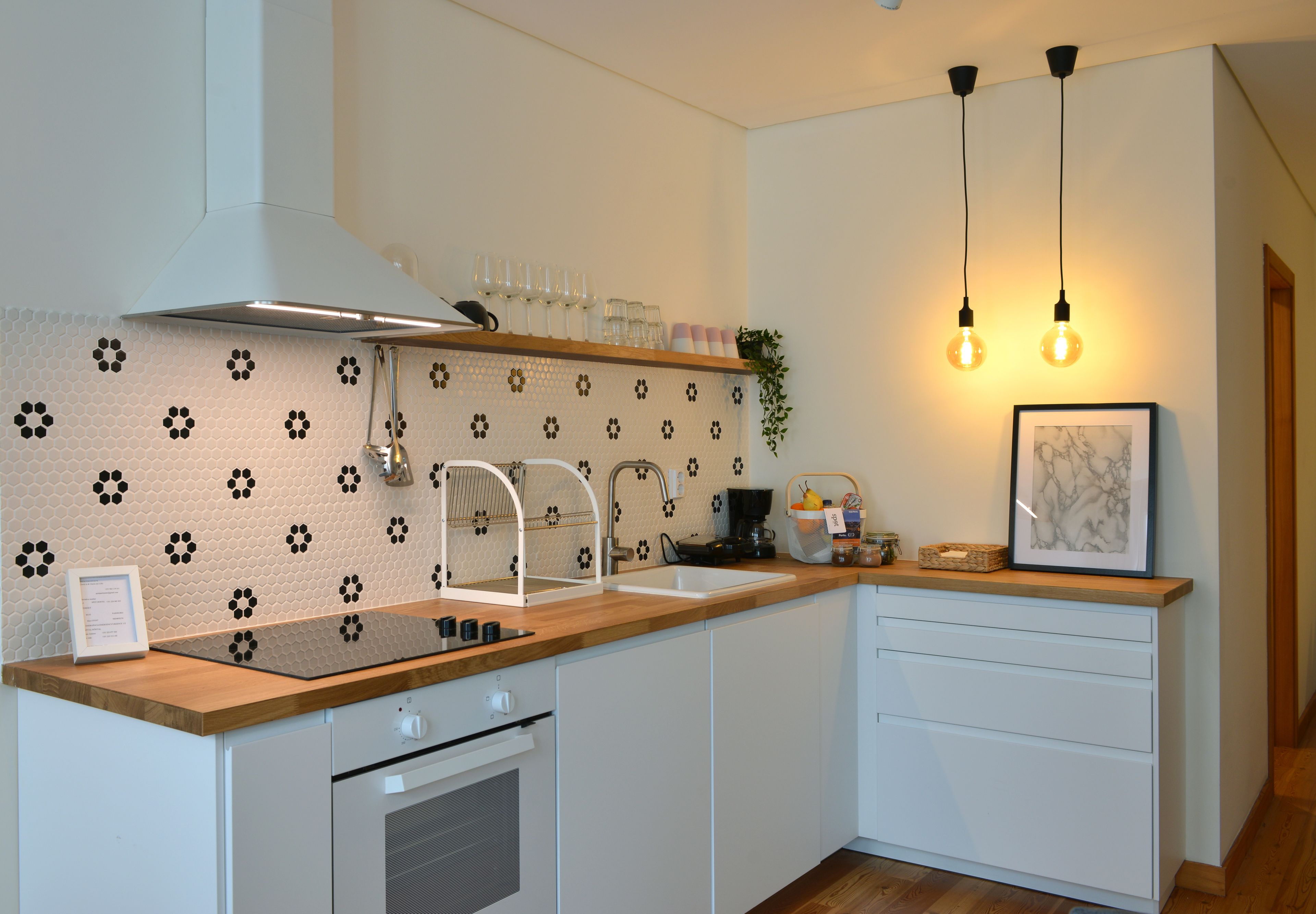 Een moderne keuken met een houten aanrecht, witte kasten, een roestvrijstalen afzuigkap, een inbouwoven, een spoelbak met een kraan en hanglampen.