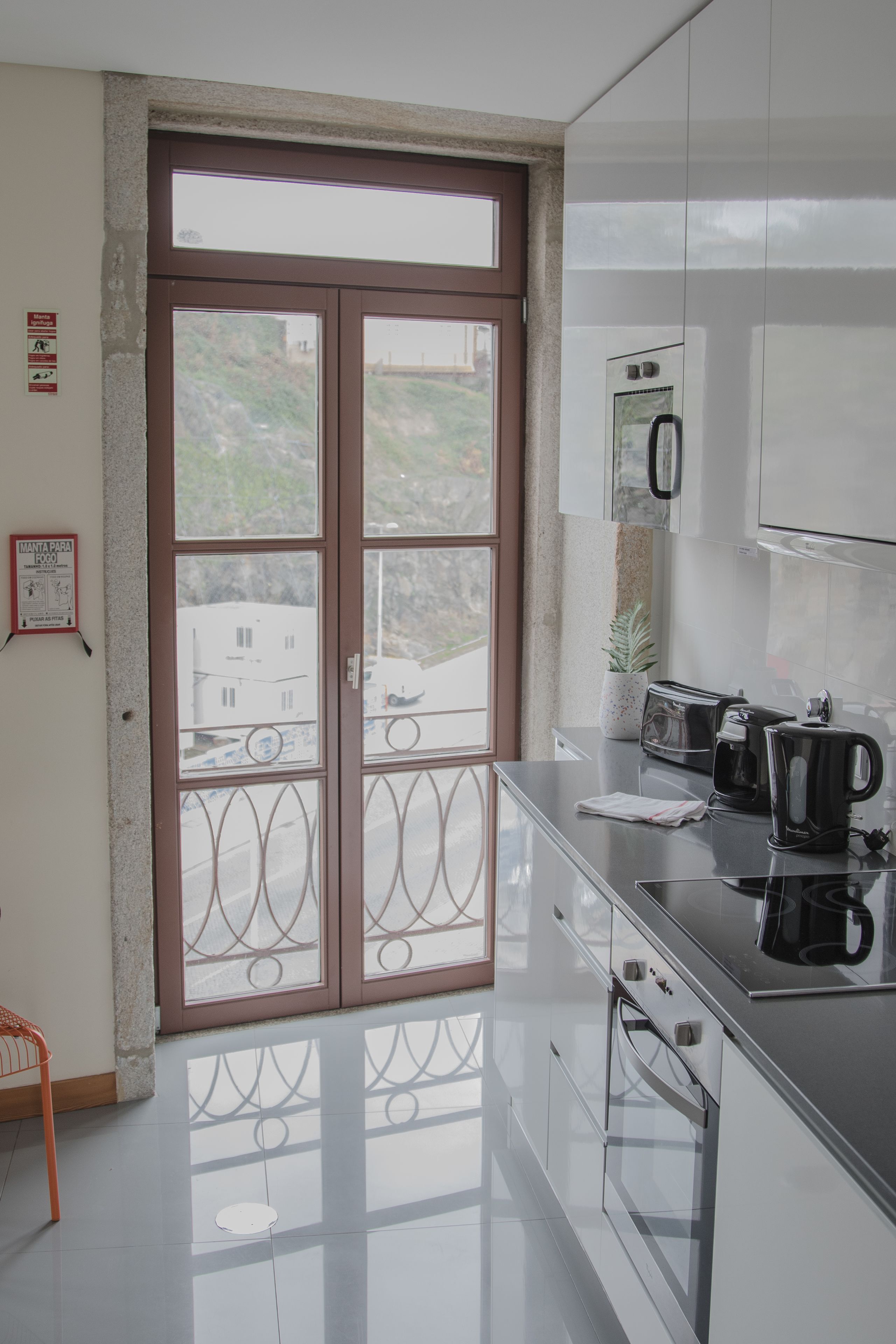 A modern kitchen with a large window, stainless steel appliances, and a clean, reflective floor.