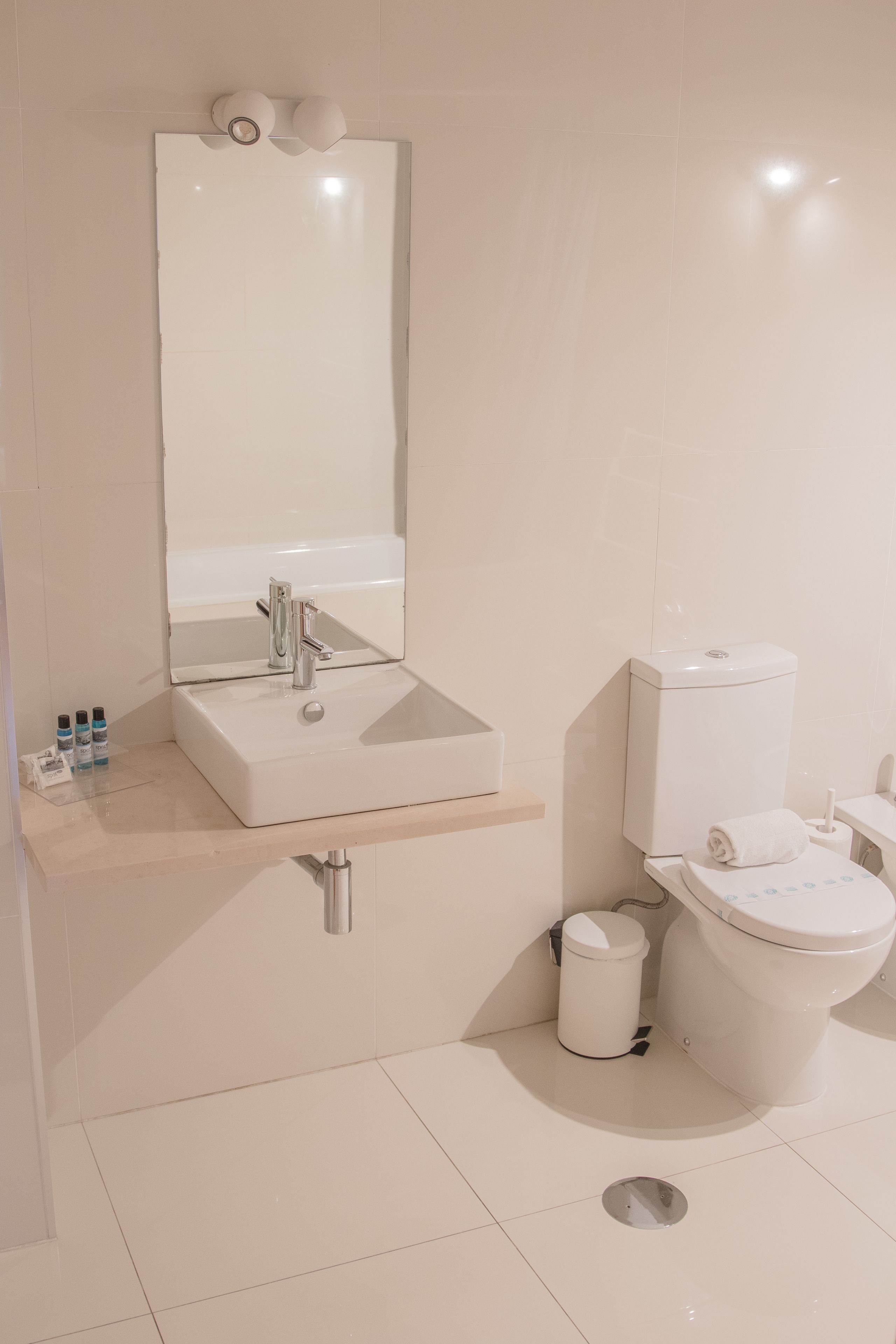 A modern bathroom with a white sink, mirror, and toilet.