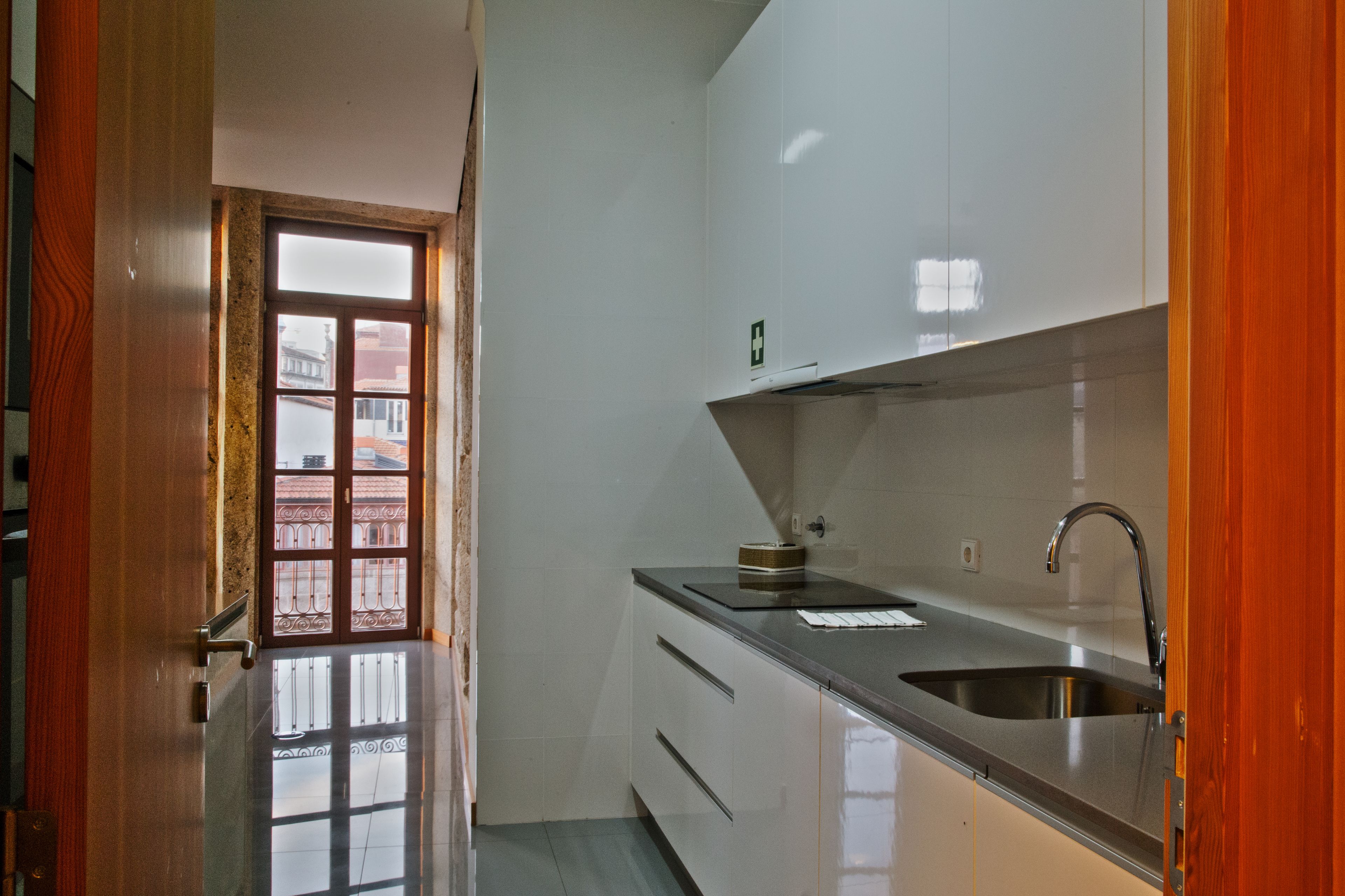 A kitchen with a stainless steel sink, a wooden door, and a view of a building through a window.