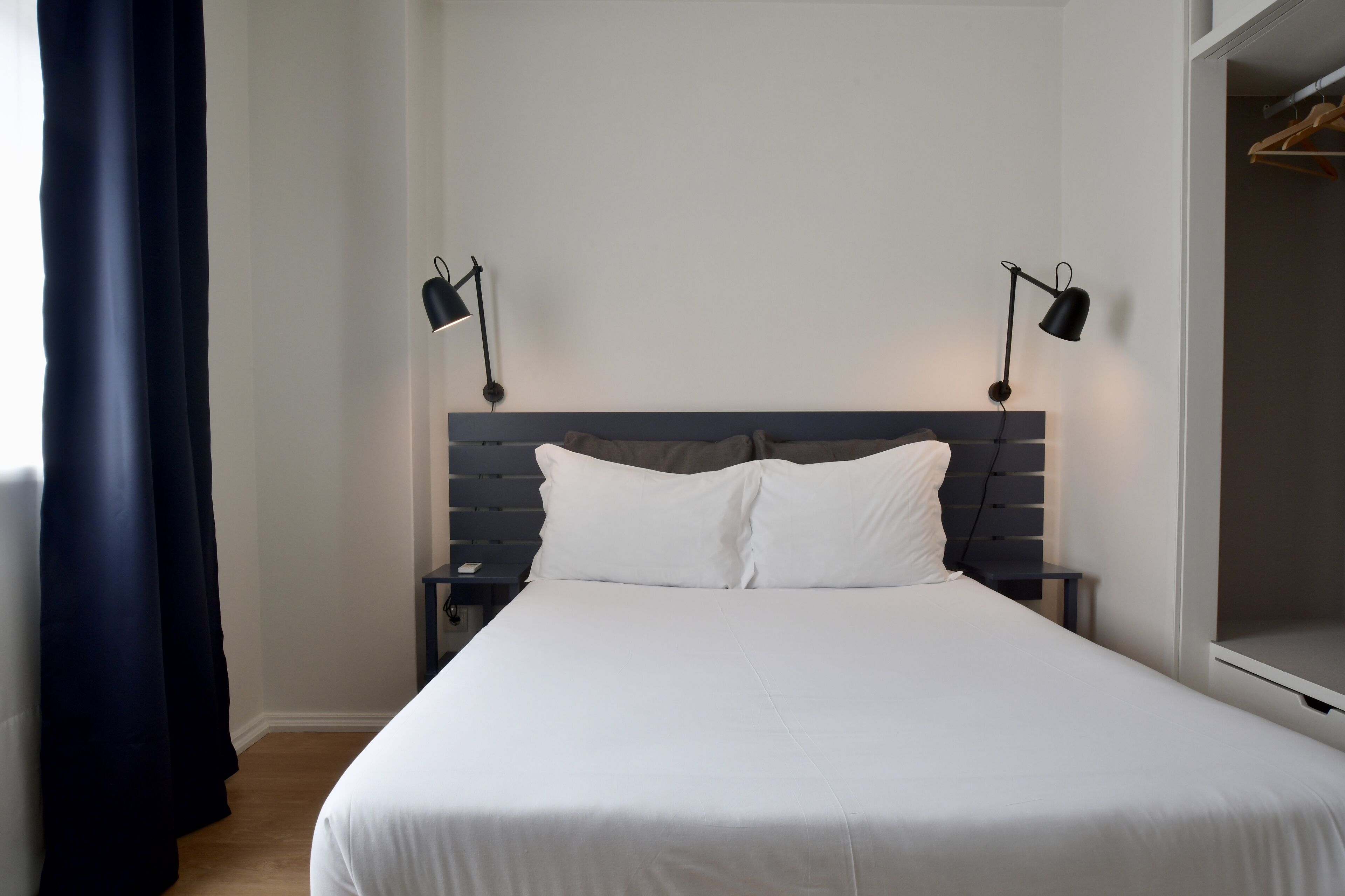 A neatly made bed with white linens, two bedside lamps, and a wooden headboard.