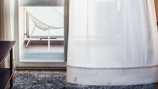 A room with a sliding glass door leading to a balcony, a white chair, and a large window with sheer curtains. - Spot Apartments (Porto)