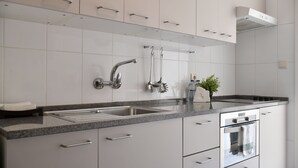 A modern kitchen with white cabinets, stainless steel appliances, and a granite countertop. - Spot Apartments (Porto)