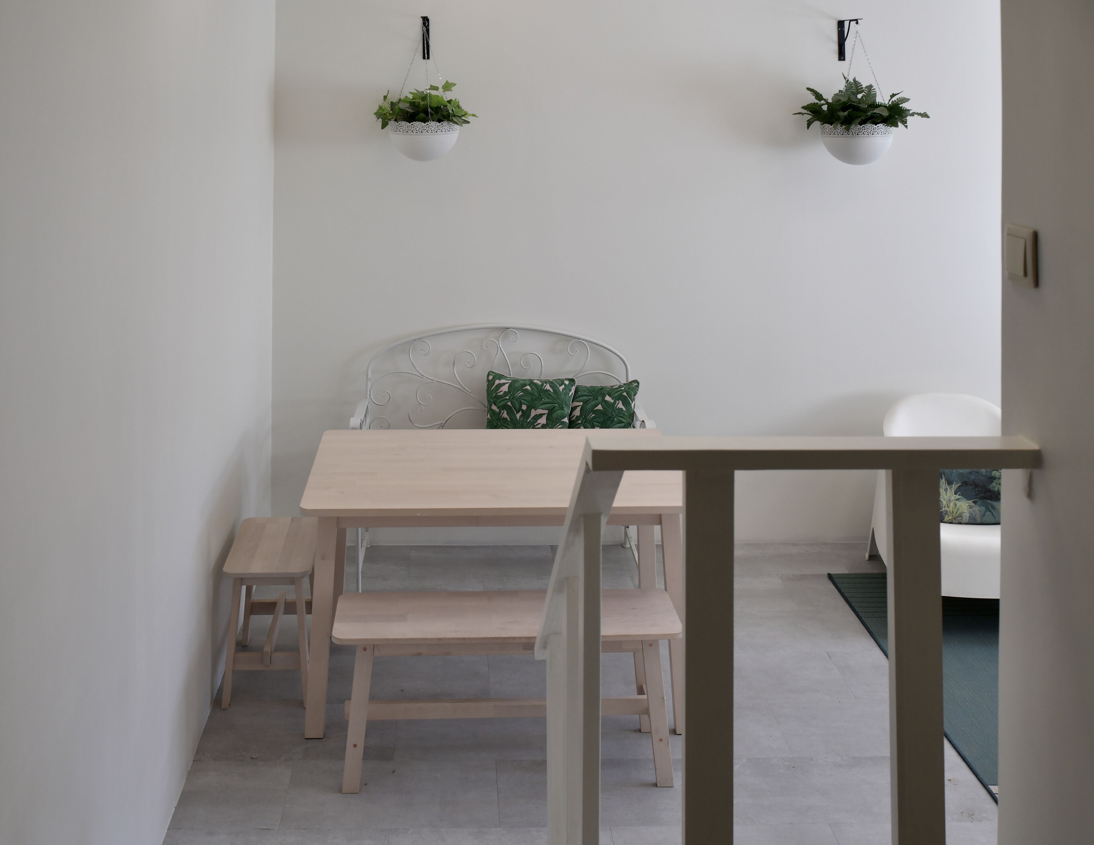 Een minimalistisch ingerichte kamer met een bed, een klein houten tafeltje en twee hangplanten.
