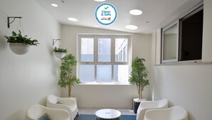 A clean, well-lit room with white walls, a large window, and two potted plants. There are two white chairs and a round table in the center. - Spot Apartments (Porto)