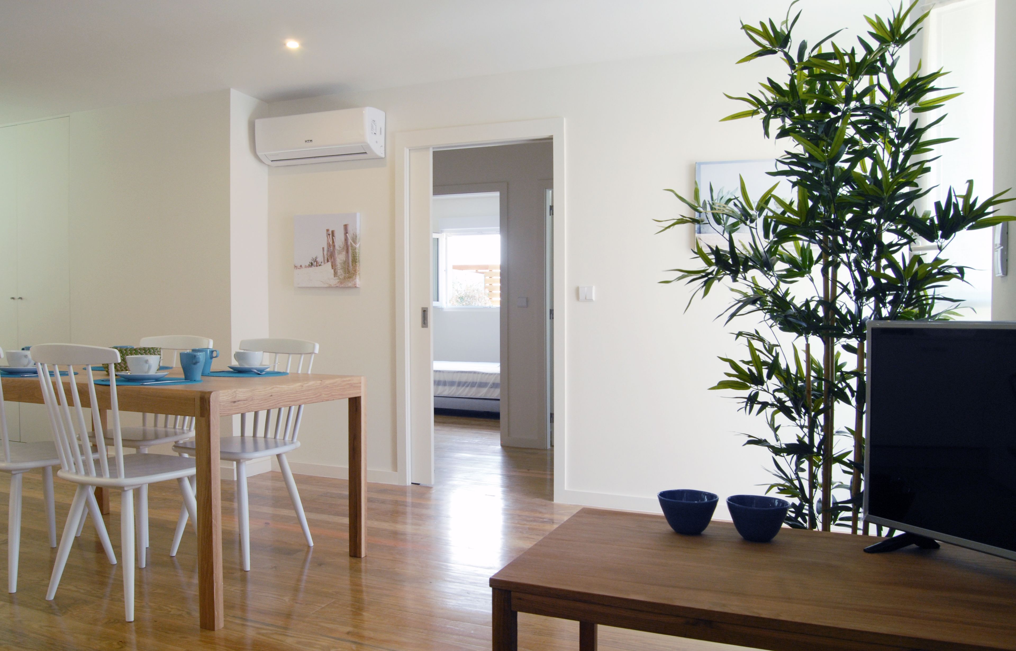 A dining area with a wooden table, white chairs, and a potted plant.