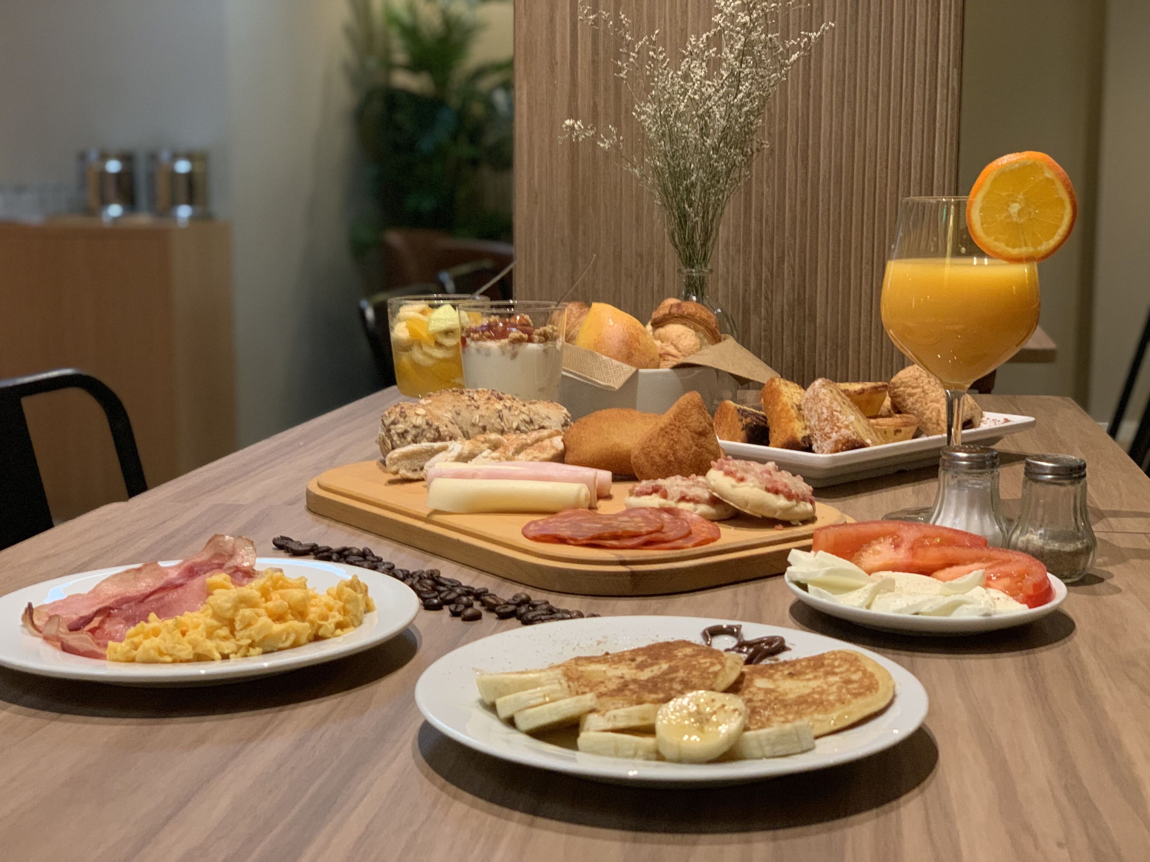 A breakfast table with various food items, including eggs, bacon, pancakes, and a glass of orange juice.