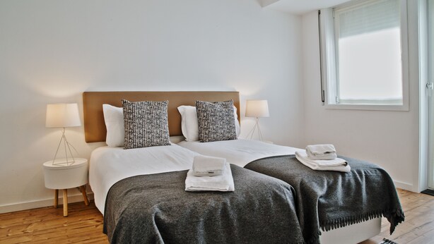 Una cama doble con cabecera de madera, dos lámparas de noche y una ventana con persianas.