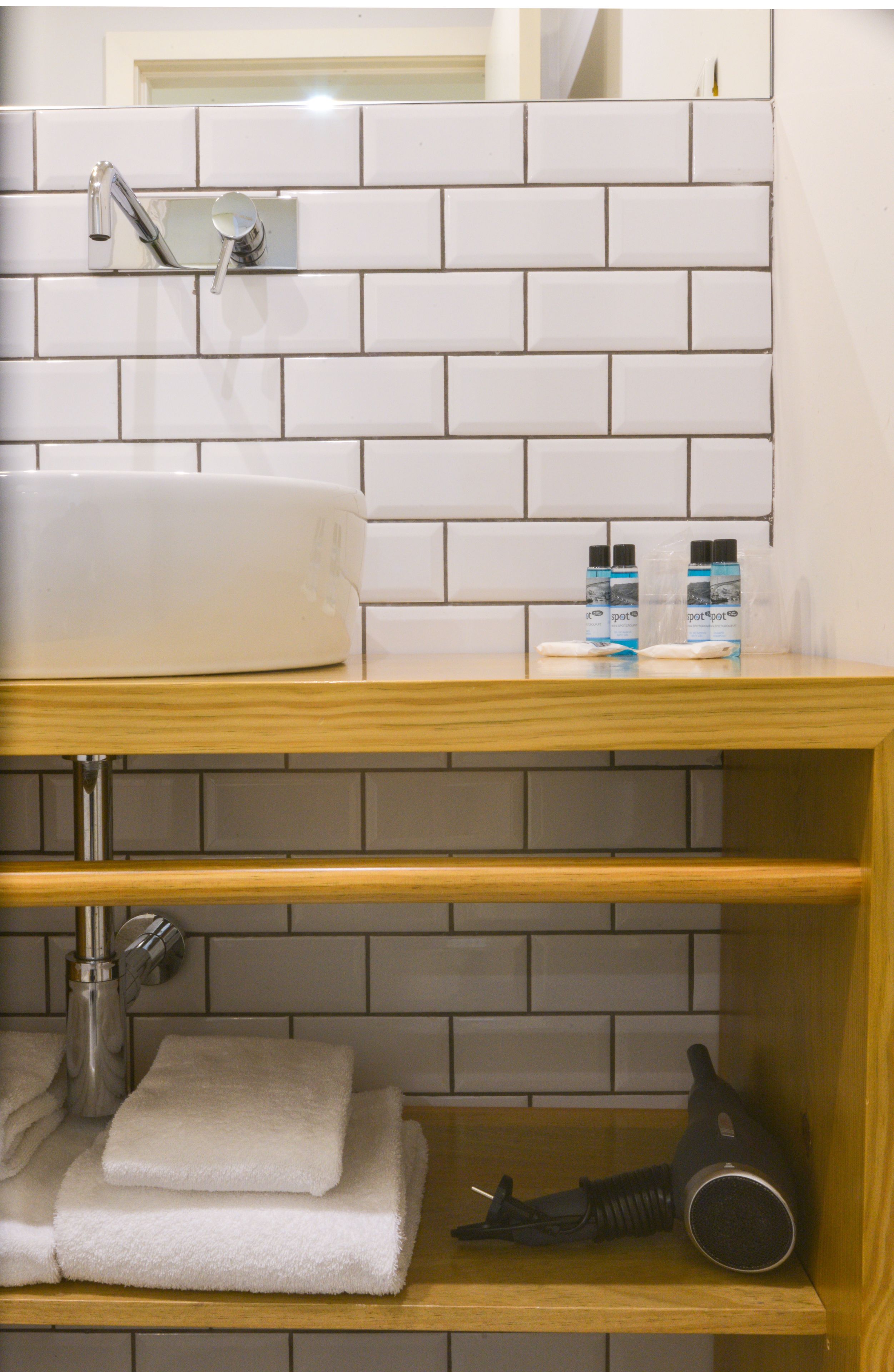 A bathroom with a white tiled wall, a wooden vanity, a sink, and a towel rack.