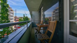 Un balcón con mesa y sillas, con vistas a un paisaje urbano con edificios y árboles.