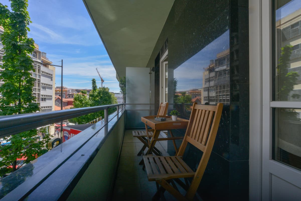 A balcony with a table and chairs, overlooking a cityscape with buildings and trees.