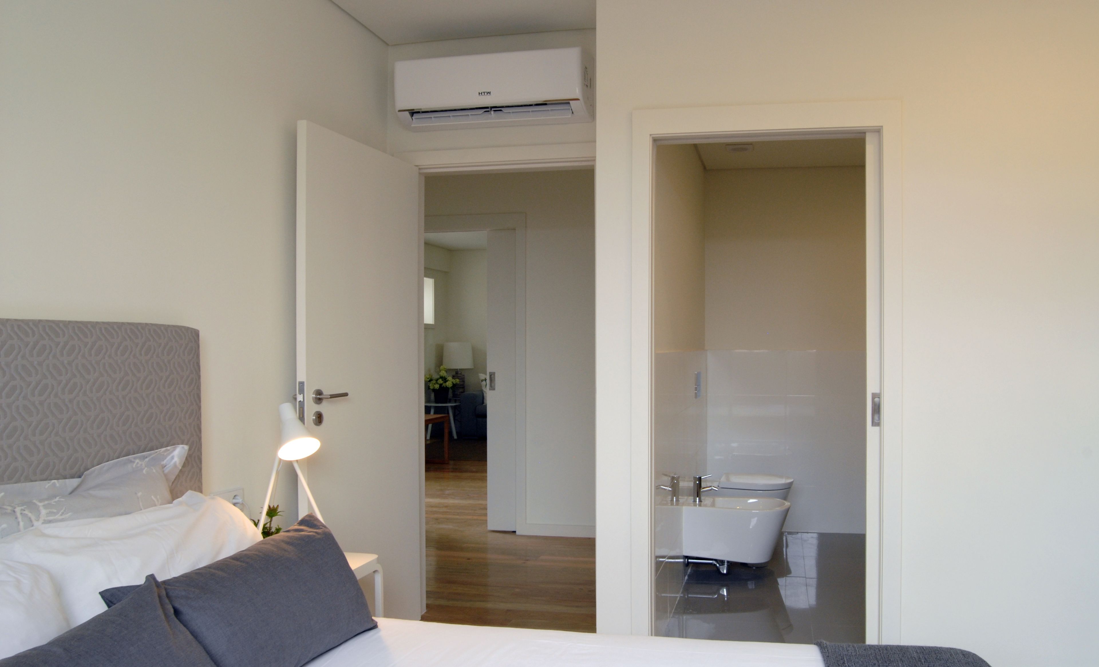 A hotel room with a bed, bedside lamp, and an open door leading to a bathroom with a bathtub and toilet.