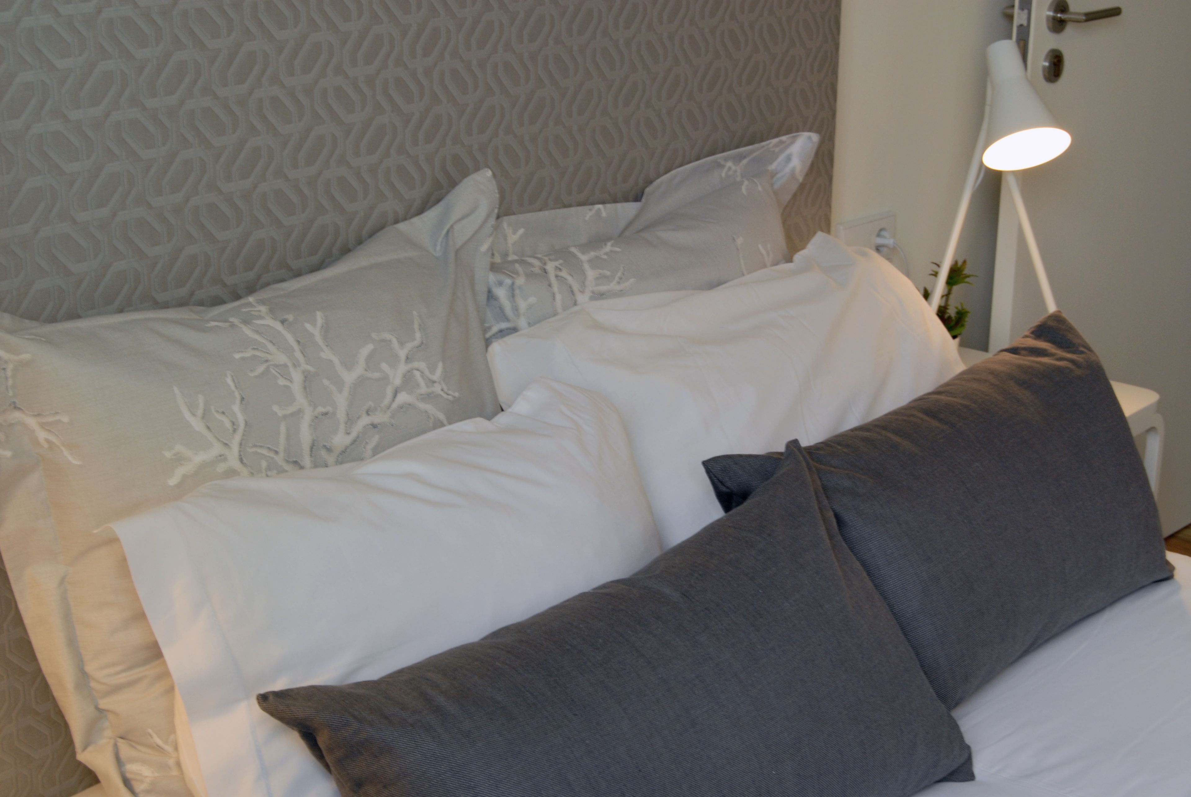 A neatly made bed with white and gray bedding, a modern lamp, and a patterned wall.