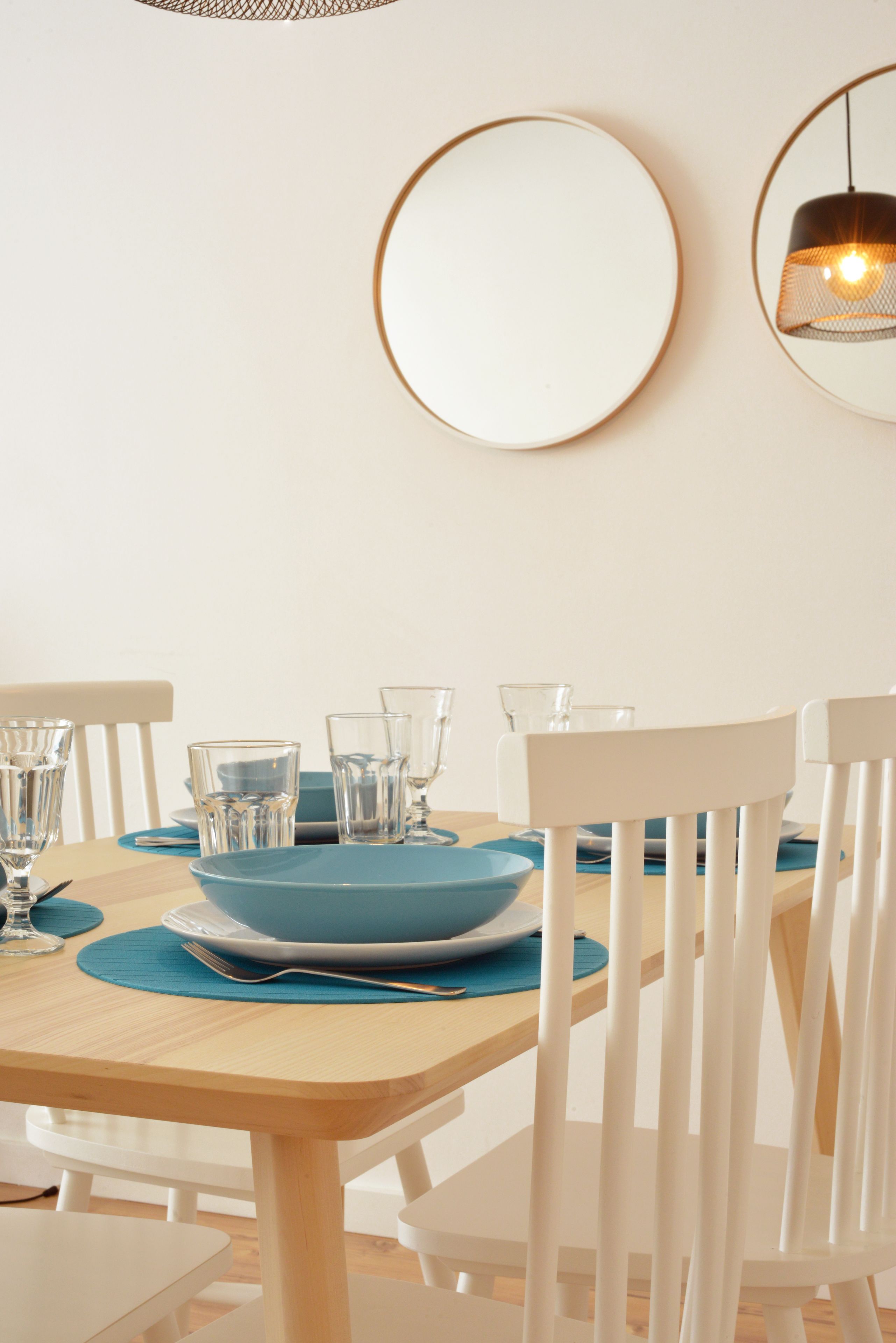 A dining table with blue plates, clear glasses, and white chairs.