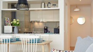 Una cocina moderna con armarios blancos, una cafetera y un comedor con mesa de madera y sillas blancas.
