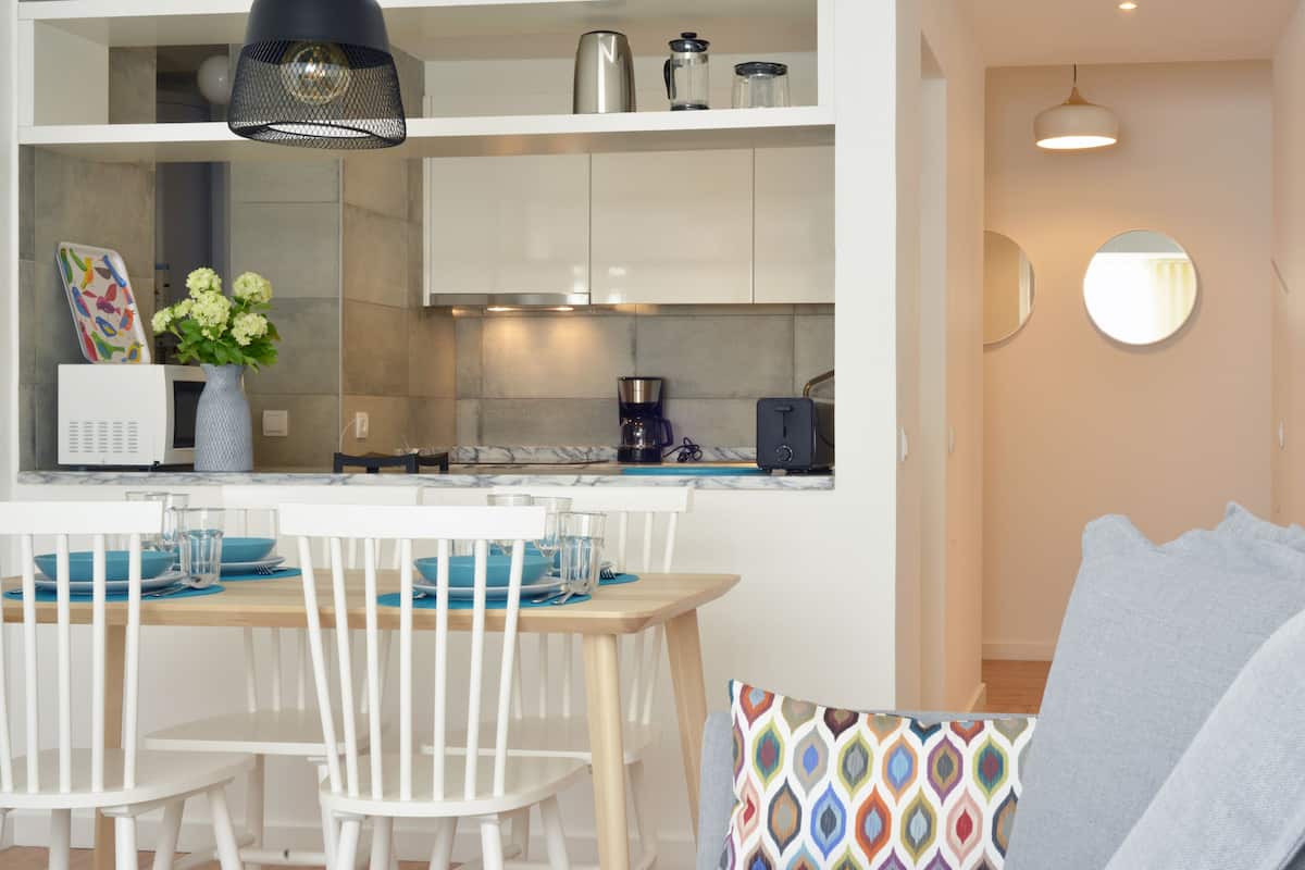 A modern kitchen with white cabinets, a coffee maker, and a dining area with a wooden table and white chairs.
