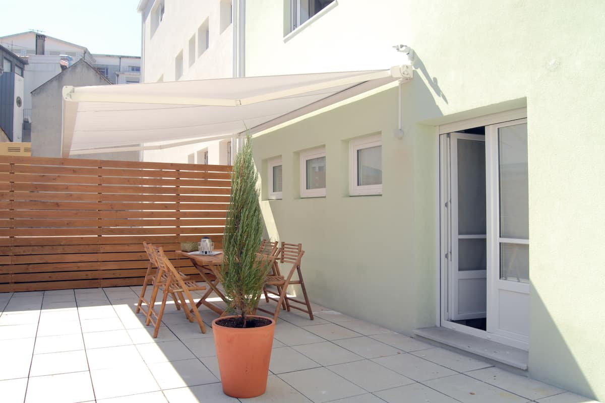 A patio with a wooden table and chairs, a potted plant, and a white awning.