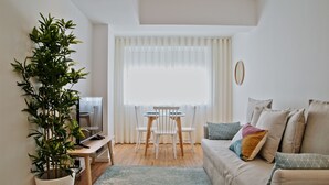 Una sala de estar con un sofá, una mesa de centro, una mesa de comedor con sillas, una planta en maceta y un televisor.