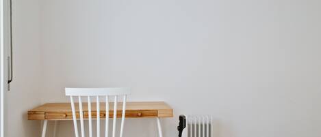 A white chair with a wooden desk, a radiator, and a power outlet on a white wall.