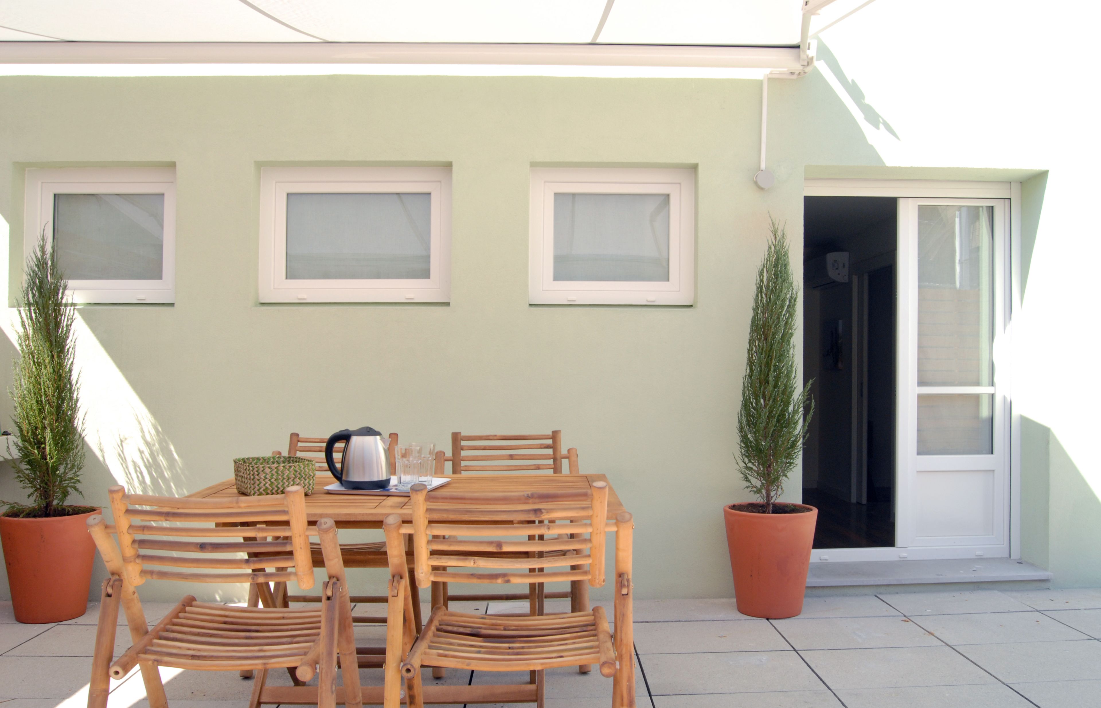 Um pátio com mesa e cadeiras de madeira, plantas em vasos e uma porta de vidro deslizante.