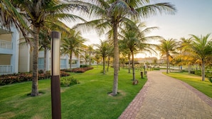 A pathway leading to a building with multiple floors, surrounded by well-maintained grass and palm trees. - Golf Ville Resort By Brisa Do Golf (Aquiraz)