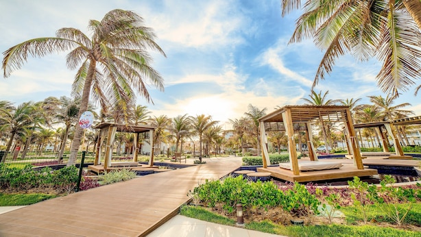 A pathway lined with palm trees and wooden gazebos, leading to a pool area with a wooden deck and surrounding greenery. - Golf Ville Resort By Brisa Do Golf (Aquiraz)