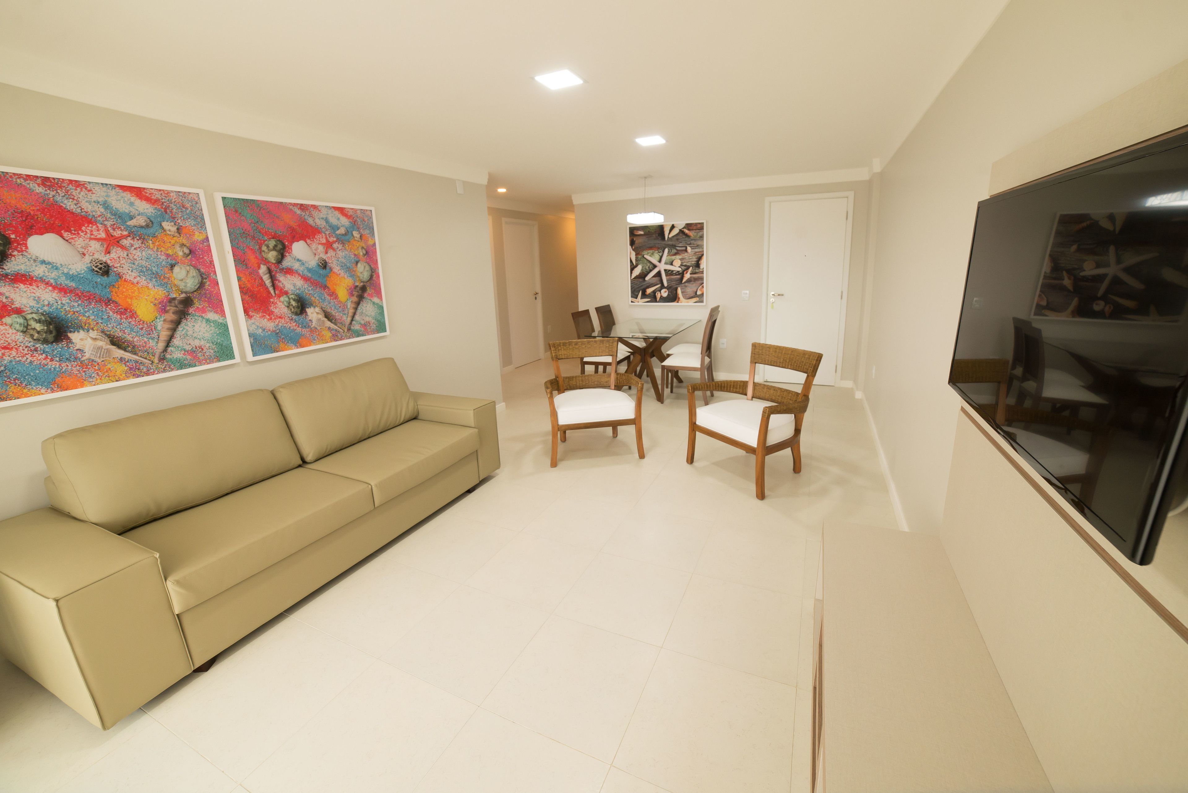 A living room with a beige sofa, a dining table with four chairs, and two abstract paintings on the wall.