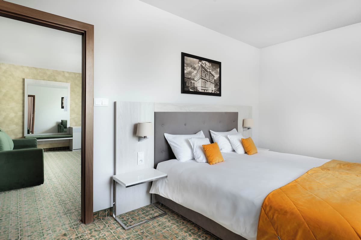 A hotel room with a bed, bedside tables, a mirror, a framed picture on the wall, and a green chair.