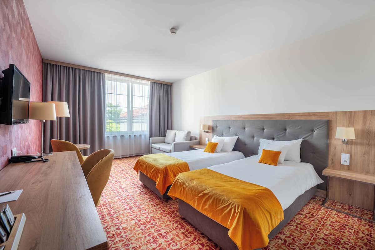 A hotel room with two beds, a desk, a television, and a window with curtains.