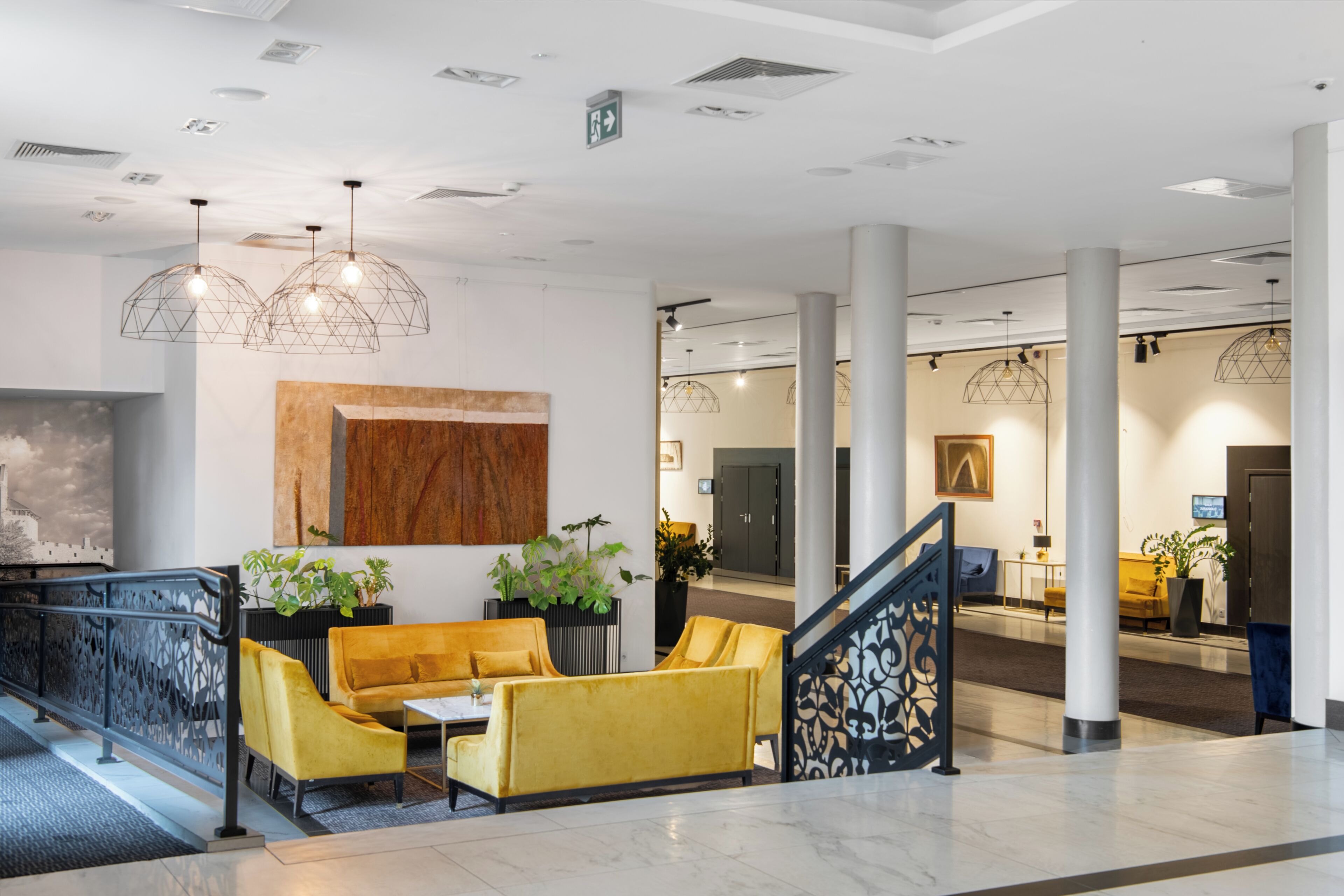 A modern lobby with a yellow sofa, geometric pendant lights, and a staircase.