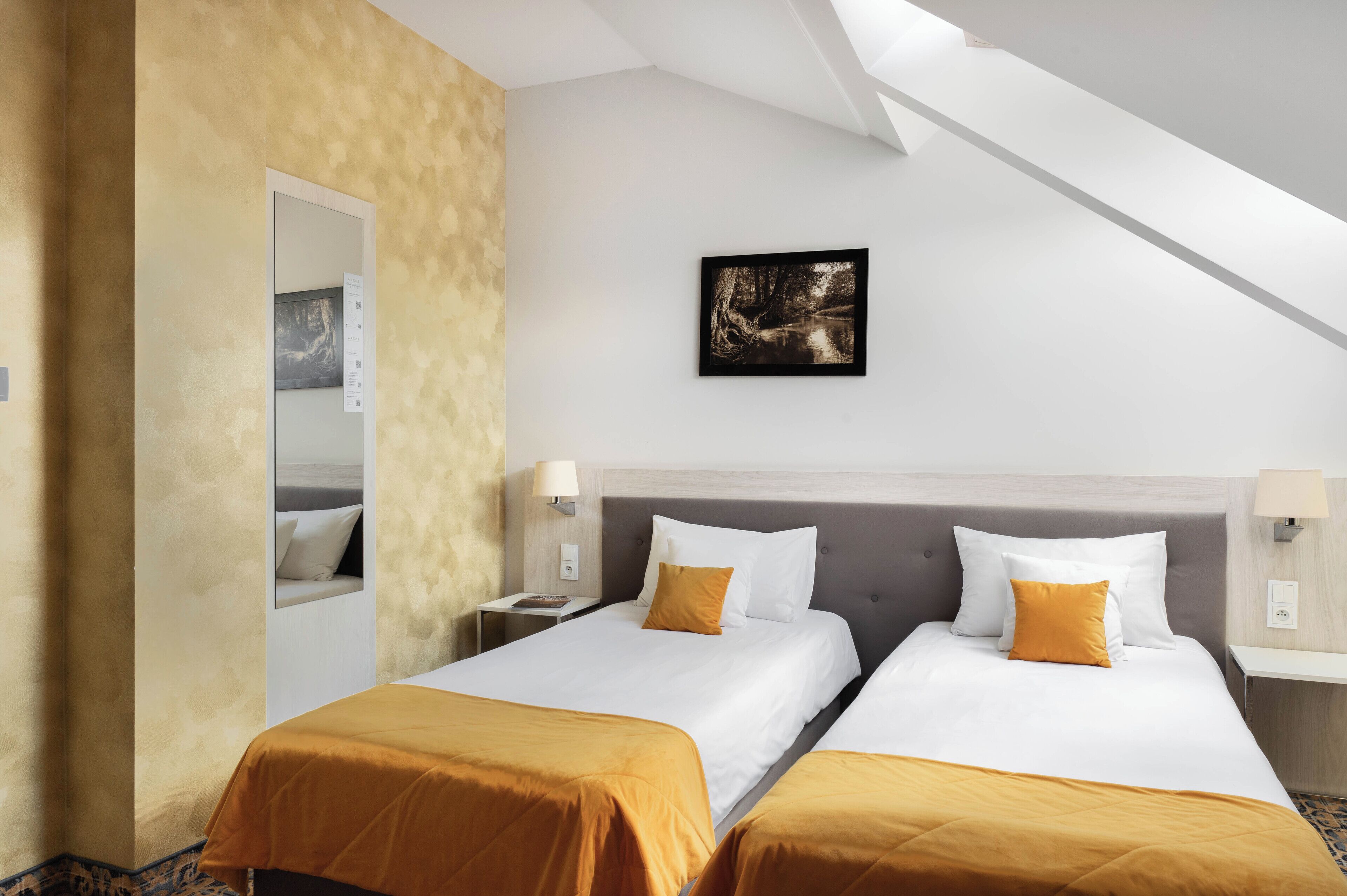 A hotel room with two beds, a large mirror, a framed picture on the wall, and a modern ceiling design.