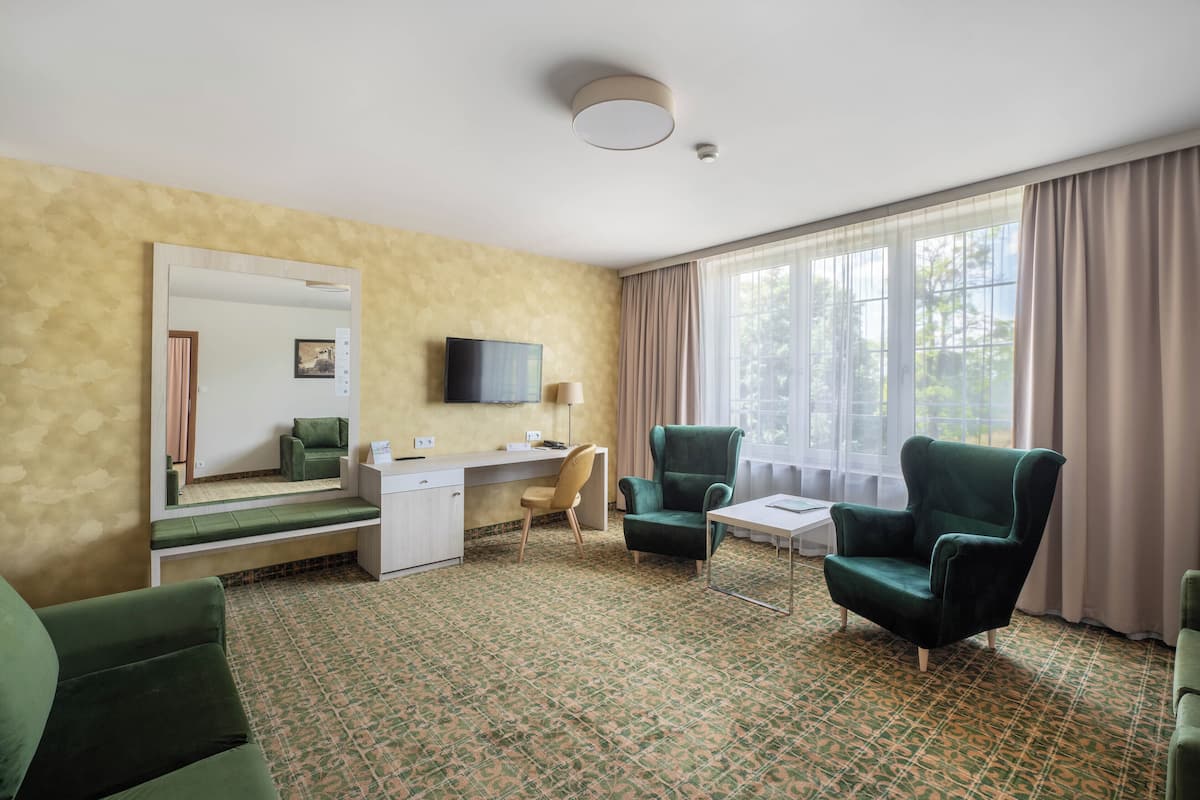 A hotel room with a desk, two chairs, a television, and a large window with curtains.