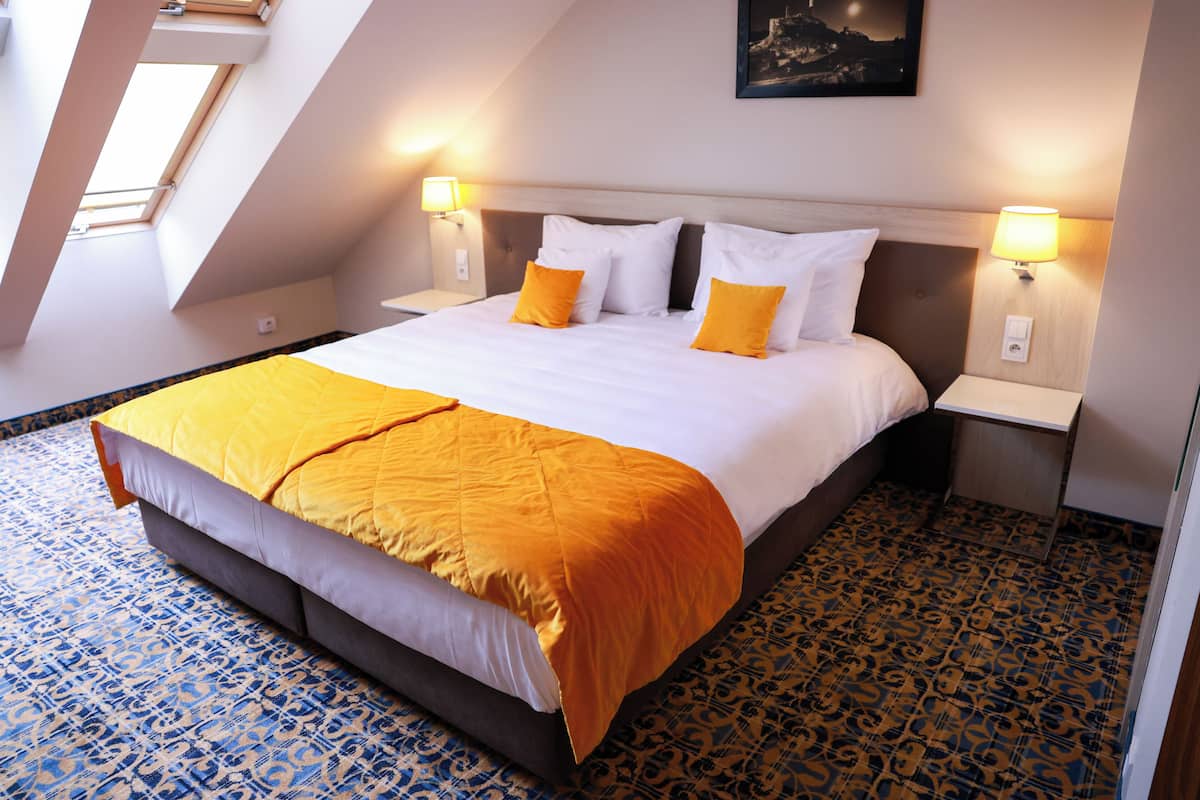 A hotel room with a large bed, two bedside lamps, a skylight, and a patterned floor.
