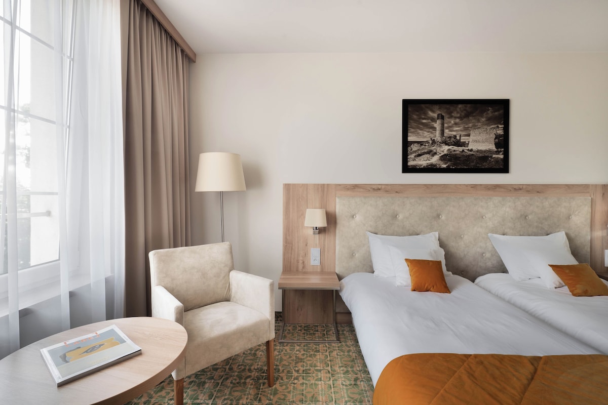 Habitación de hotel con cama, una silla, una mesa, una lámpara y un cuadro en la pared.