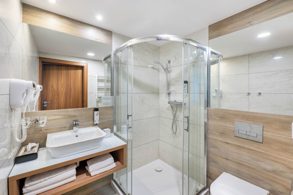A modern bathroom with a glass-enclosed shower, a sink with a mirror, and a wooden vanity.