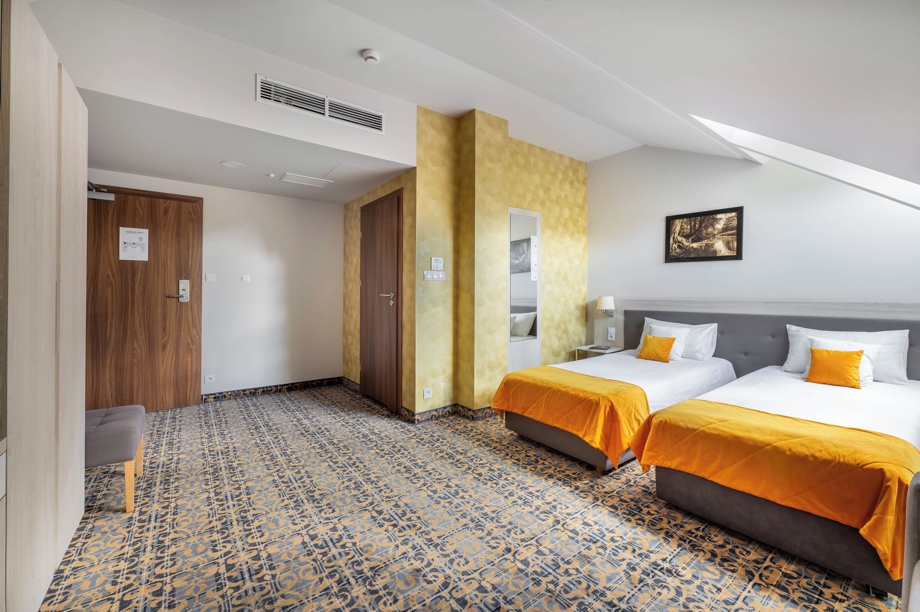 Een hotelkamer met twee bedden, een bank, een kamer met een patroon en een schilderij aan de muur.