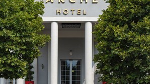 Exterior del hotel Arche, con entrada despejada, amplias columnas y un cartel sobre las puertas.
