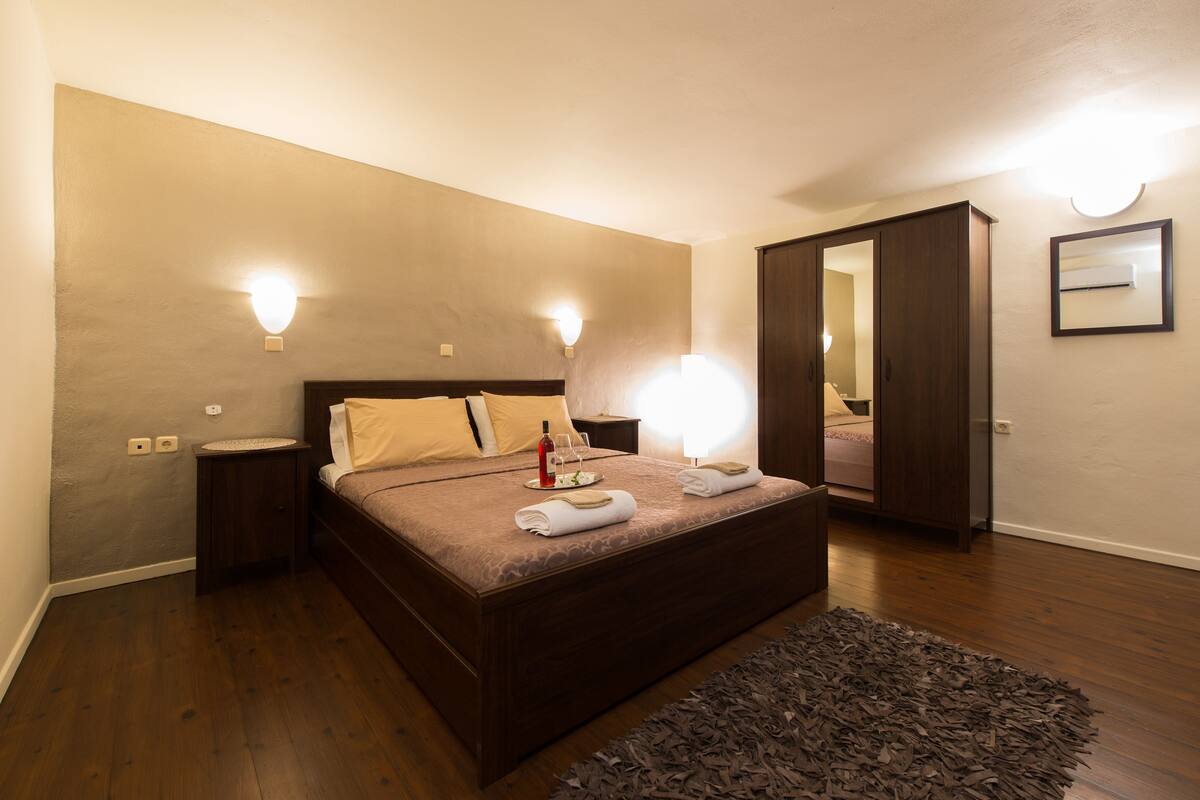 Un dormitorio con una cama grande, lámparas de noche, una mesita de noche, un espejo y suelo de madera.