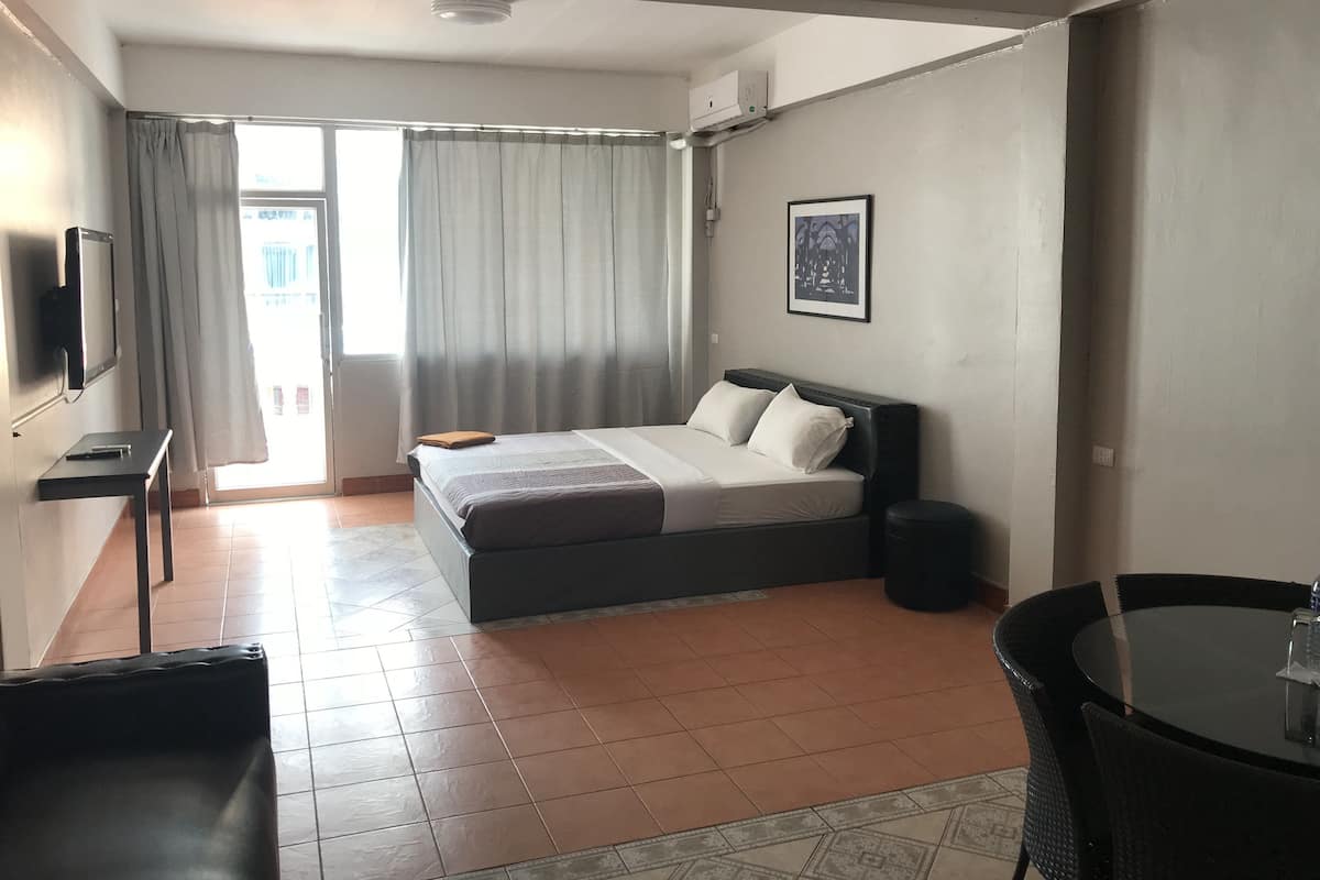 A hotel room with a bed, a small table, a chair, a TV, and a window with curtains.