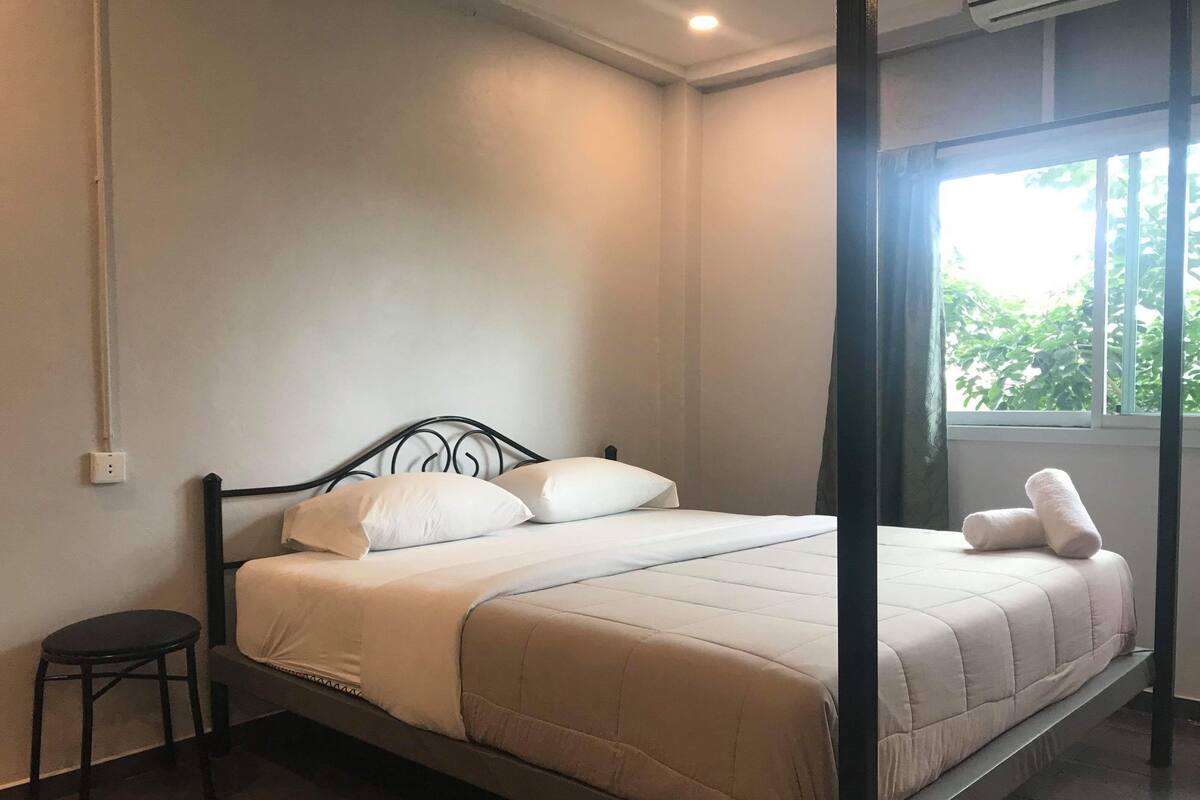 A single bed with a metal frame, white bedding, and a window with curtains.
