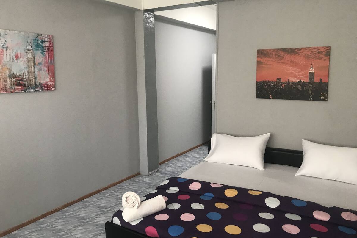 A hotel room with a bed, a polka dot blanket, a rolled towel, a cityscape painting, and a painting of a city skyline.
