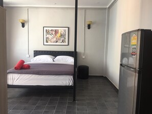 Un dormitorio con una cama, un cuadro abstracto enmarcado, un refrigerador y un cubo de basura.