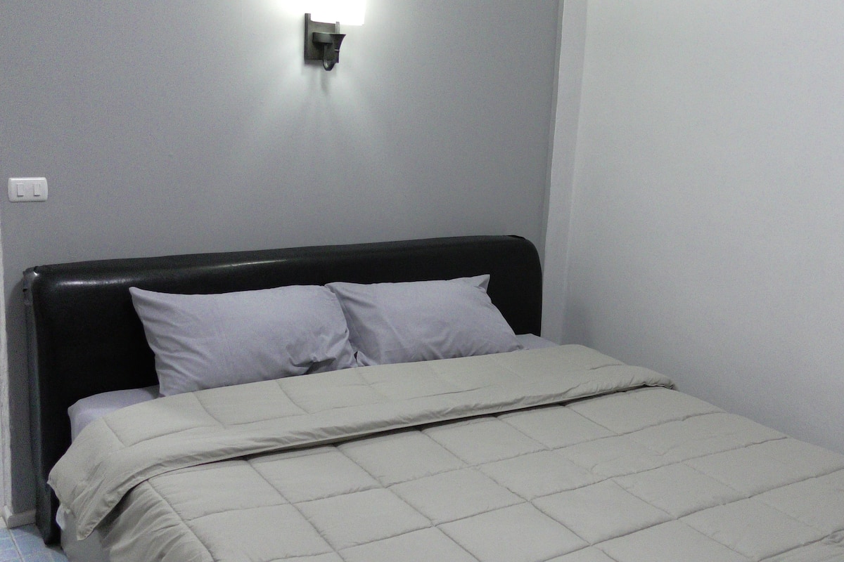 A bed with a black headboard, two pillows, and a light-colored quilt.