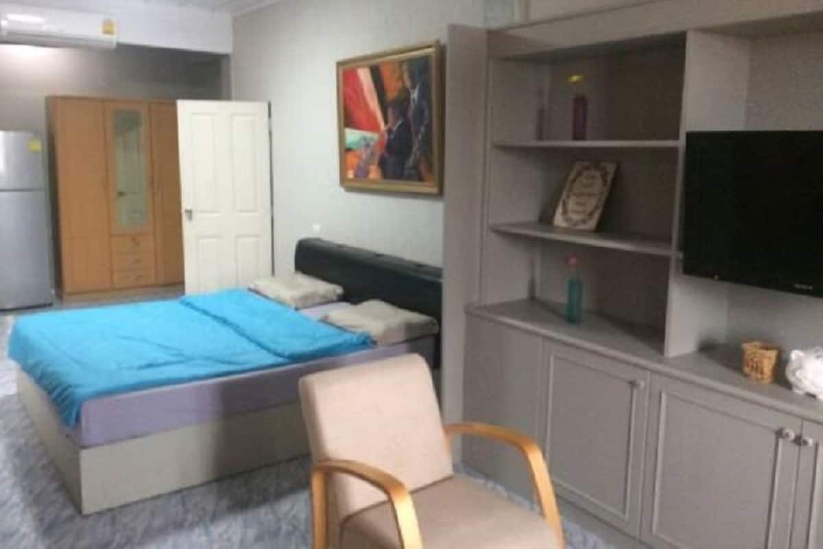 A bedroom with a bed, a chair, a wardrobe, a shelf with a television, and a painting on the wall.