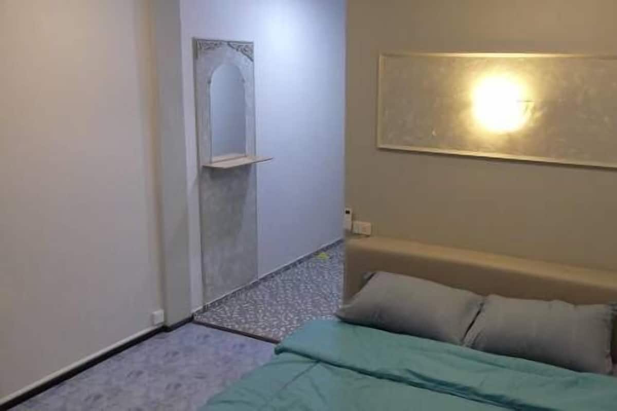 A small, narrow room with a bed, a wall-mounted light, and a small alcove with a mirror.