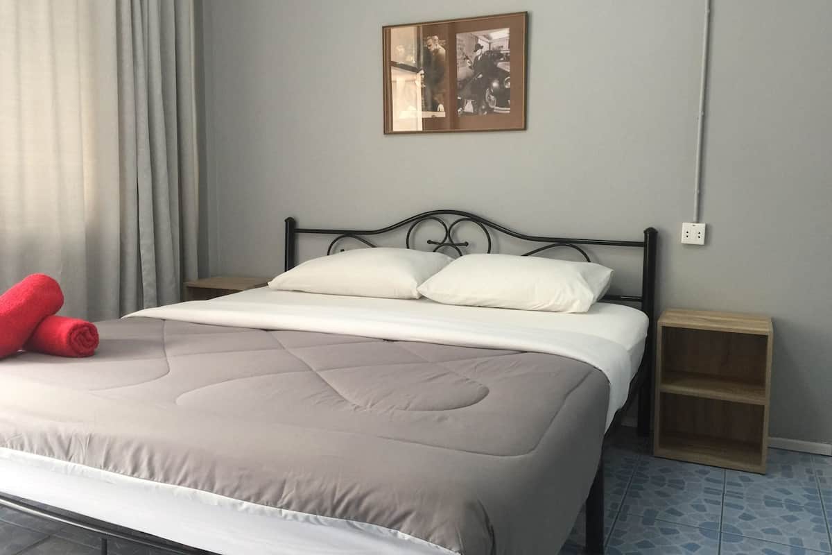 A neatly made bed with a beige comforter and white pillows, a red towel on the left, and a small wooden nightstand beside it.